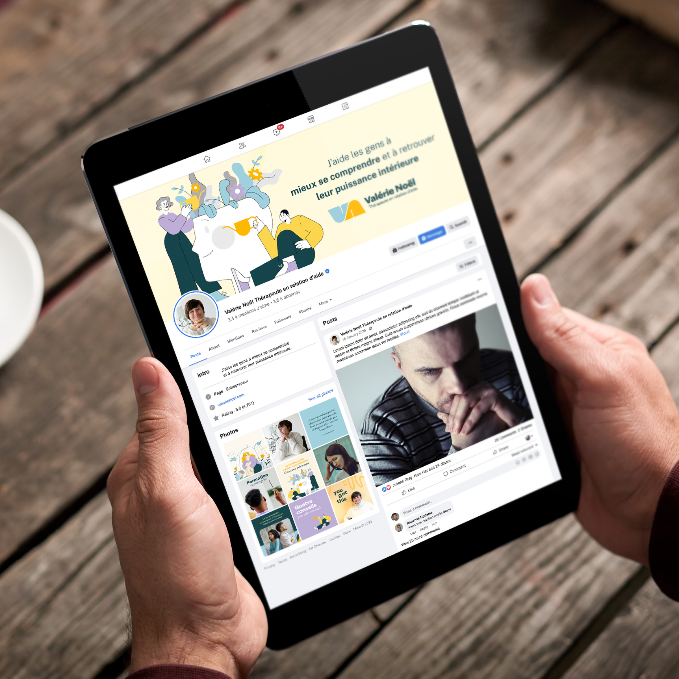 Personne tenant une tablette affichant une page de profil Facebook avec une photo de couverture illustrée en jaune et vert, sur fond de table en bois.
