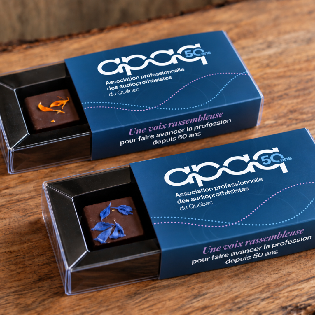 Deux boîtes contenant chacune un chocolat orné de décorations, portant une étiquette commémorative du 50e anniversaire de l'Association professionnelle des audioprothésistes du Québec.